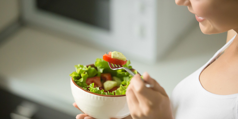 Bowl of fresh green salad hold in female hands